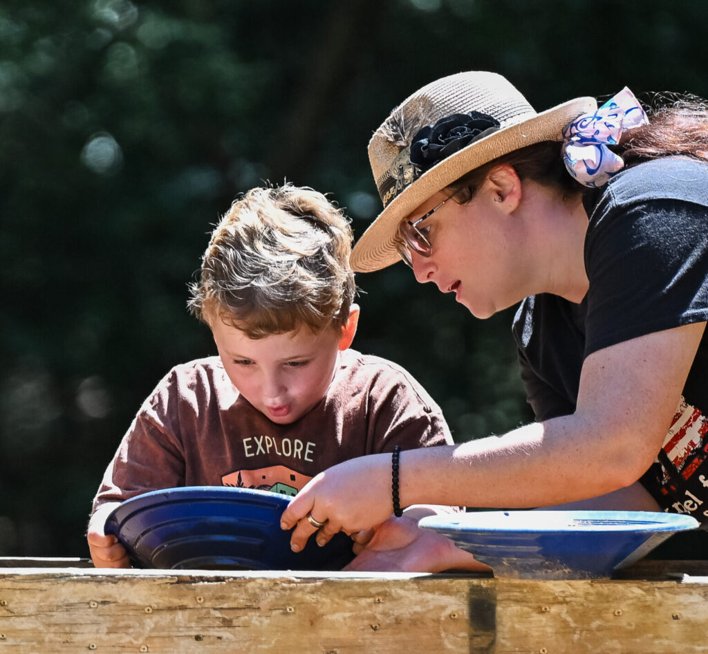 A woman and young boy look down in awe as they pan for gold at a historic site